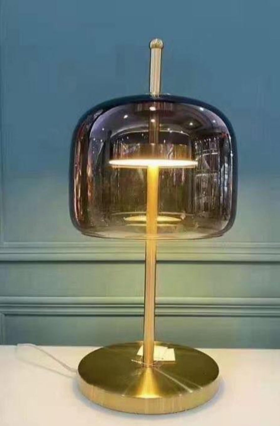 A contemporary style bed table lamp with a geometric glass shade and a gold-colored base, illuminated.