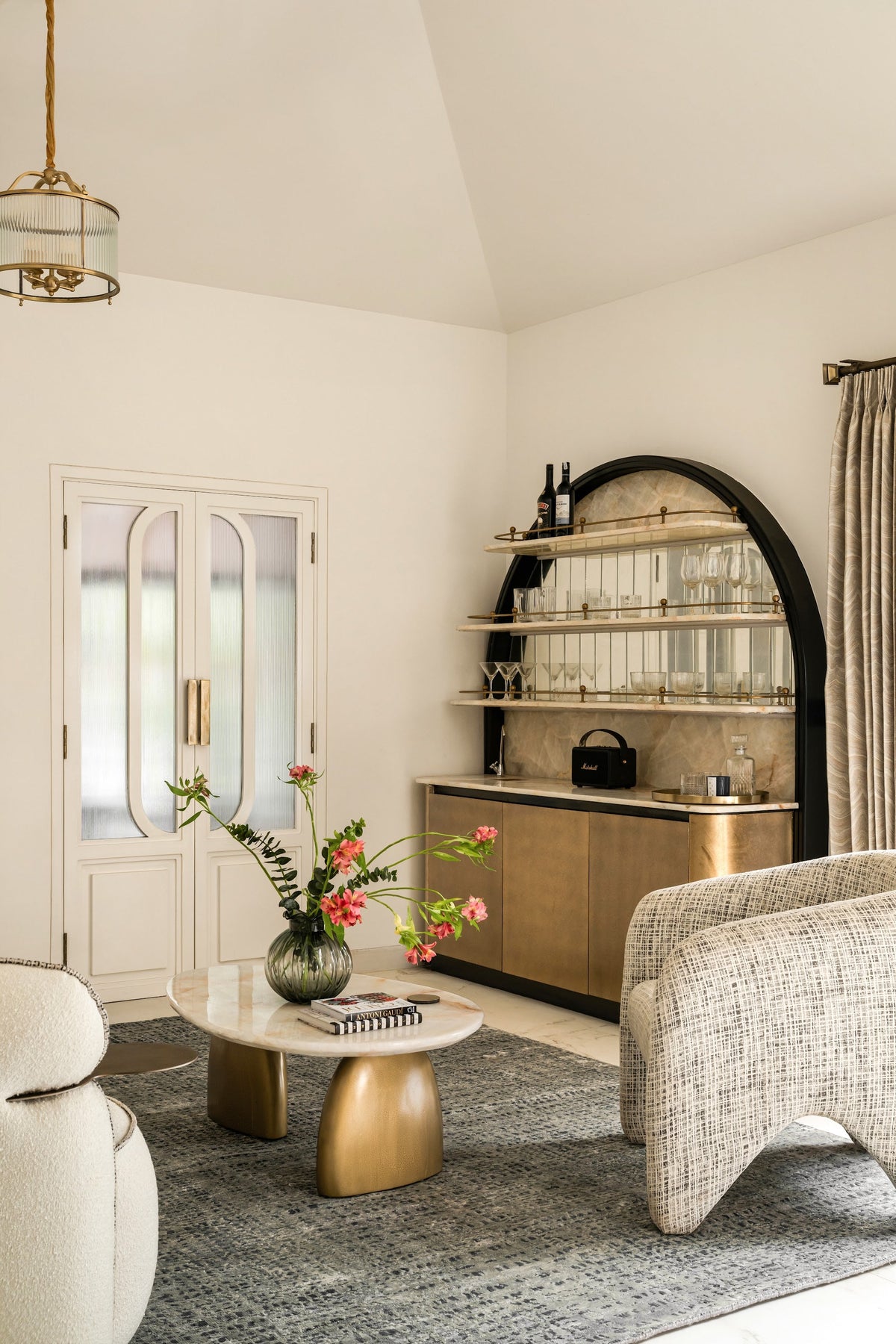 A boucle armchair beside an arched bar unit with brass shelves