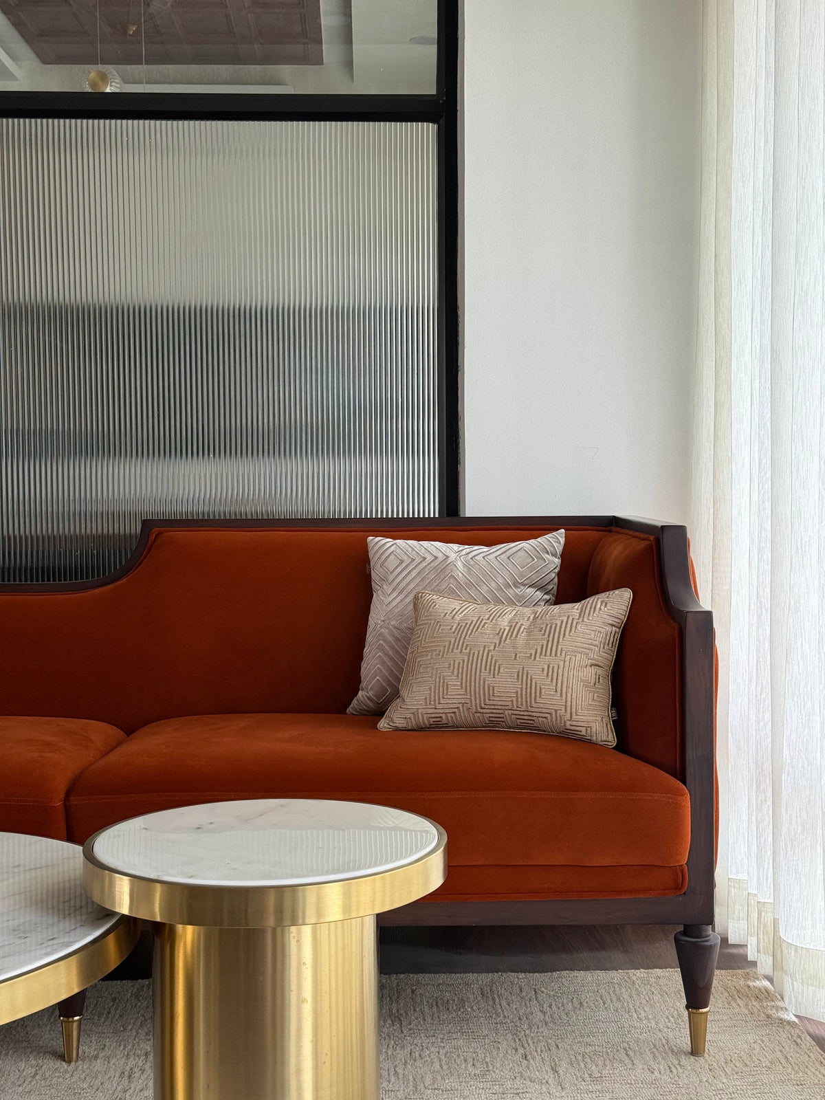 A rust velvet sofa beside brass and marble side tables
